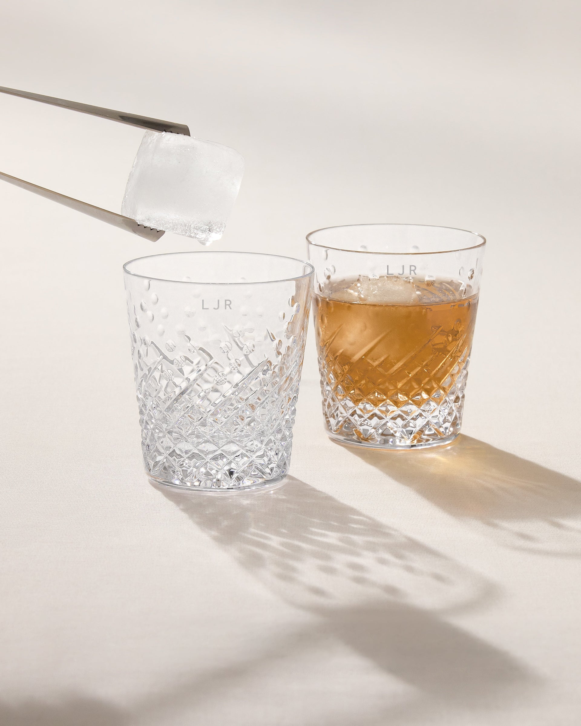 Two crystal glasses, one filled with a clear liquid and the other with a amber liquid, on a light background.