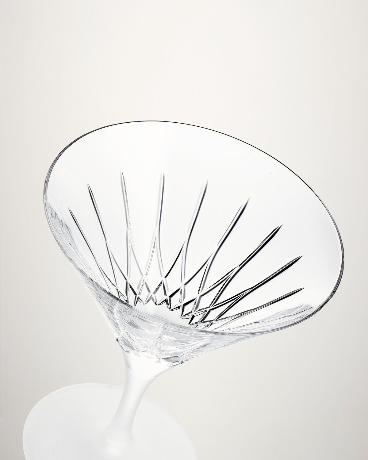 A clear cut-glass cocktail coupe with a wide, conical bowl and a slender stem, photographed on a clean light gray background.