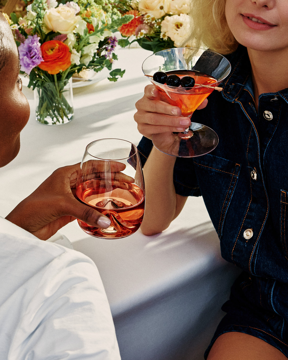 Two people holding cocktails at a table with flowers in the background