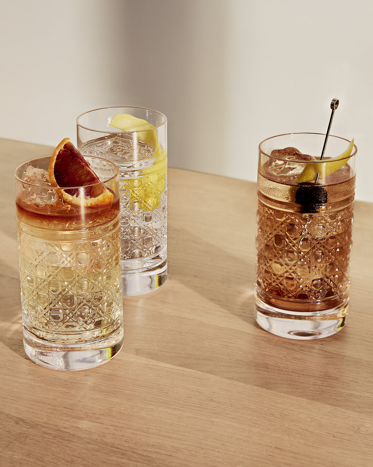 Three cocktails in glass tumblers on a wooden surface with a neutral background