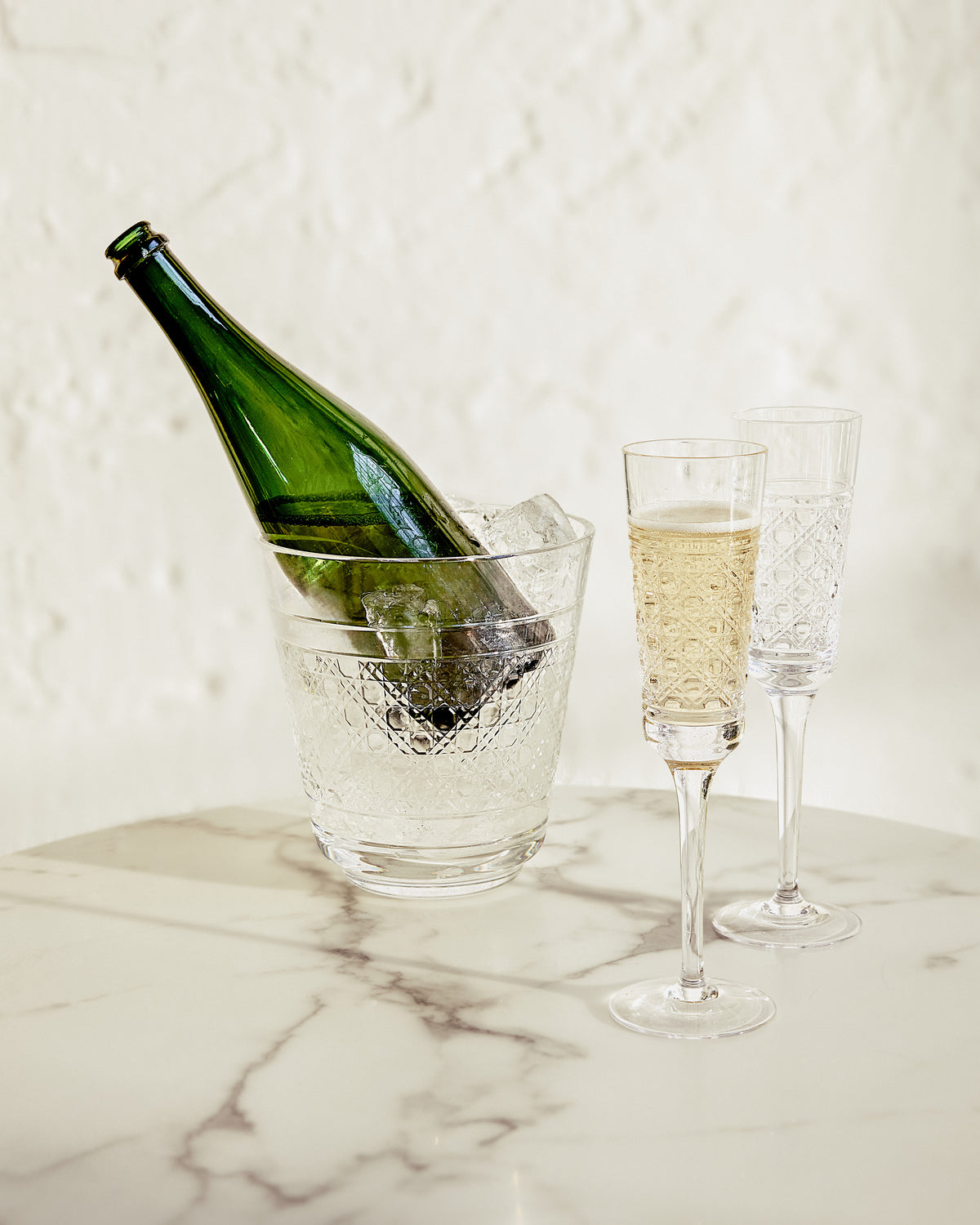 Bottle of champagne in an ice bucket with two flutes on a marble surface