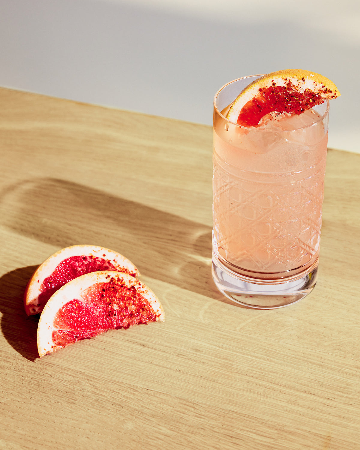 Glass of pink cocktail with grapefruit slice on a wooden surface