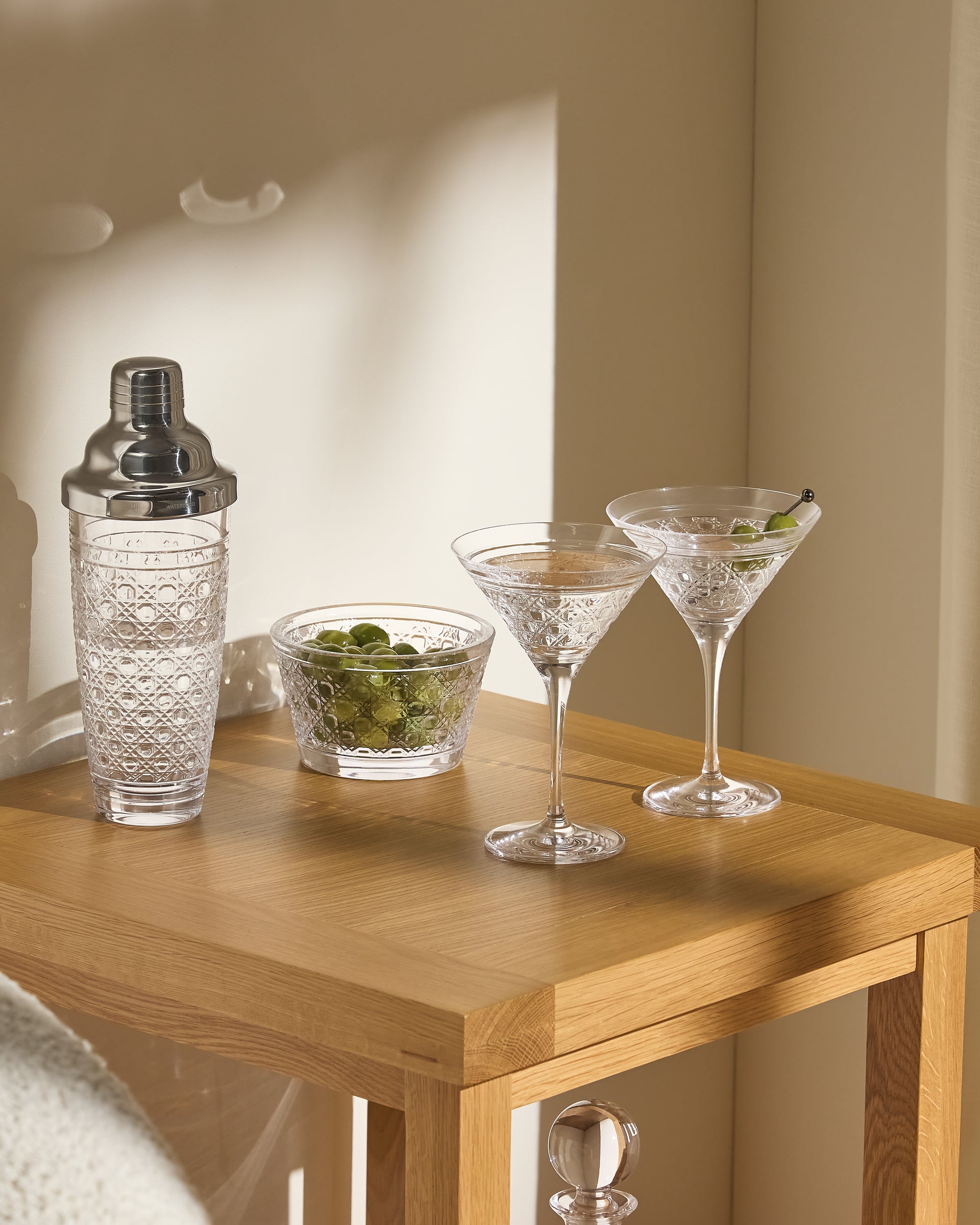 Cocktail shaker, two martini glasses with olives on a wooden table.